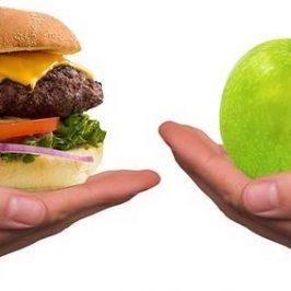Twee handen met een hamburger en fruit