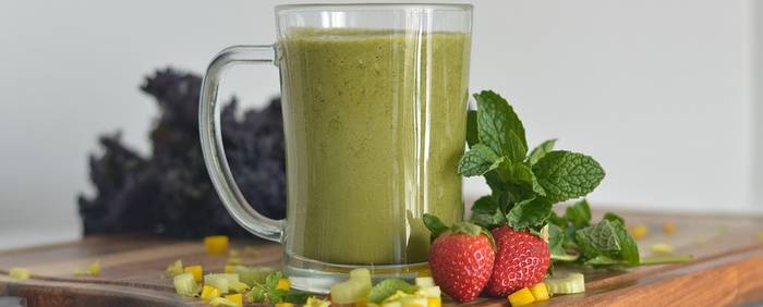 Een gezonde groene smoothie met een aardbei er naast